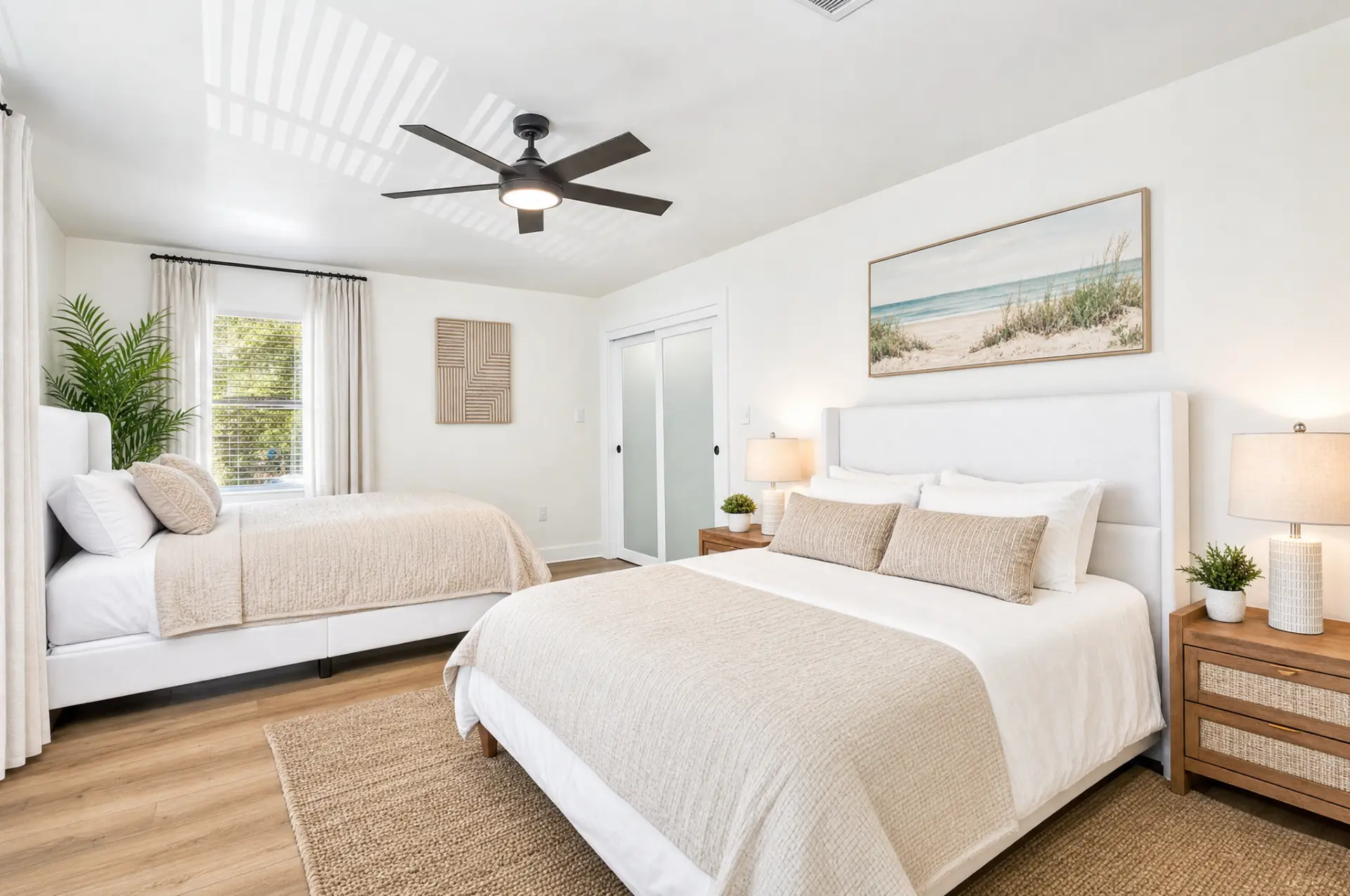 Spacious coastal bedroom with two beds, neutral linens, and warm wood flooring